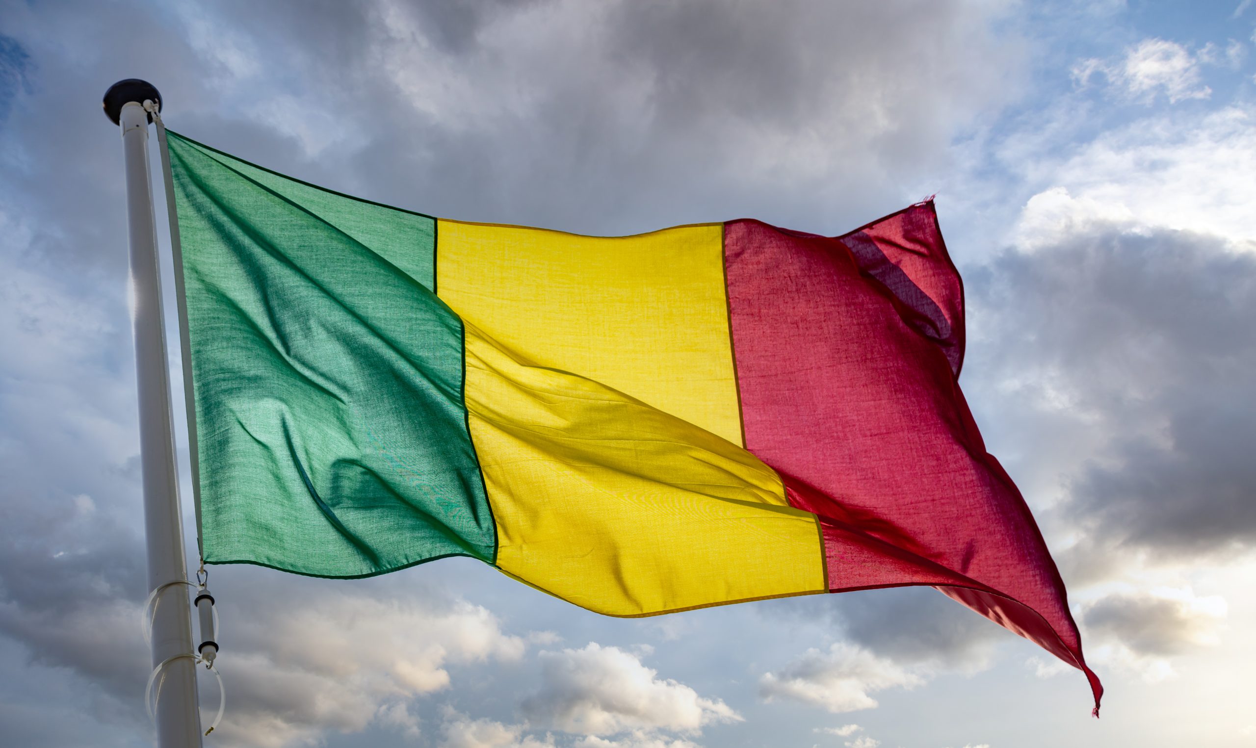 Mali sign symbol. Mali national flag on a pole waving against cloudy sky background.